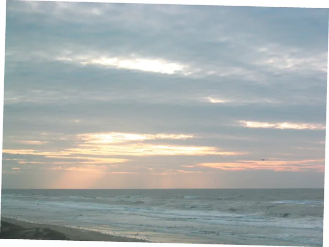 De zee bij ondergaande zon, met licht dat door de wolken valt.